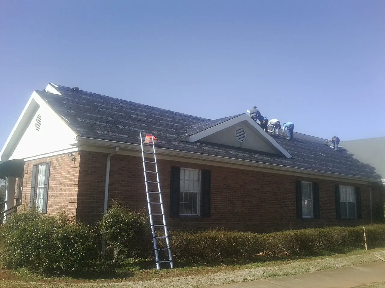 Crew tearing shingles off a brick ranch roof with a ladder set — Metal Roof Repair work by our crew in Powhatan Point
