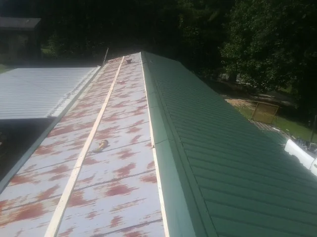 Old rusted panels beside newly installed green metal roofing — Wind Damage Roof Repair by Roofing Brothers in Powhatan Point