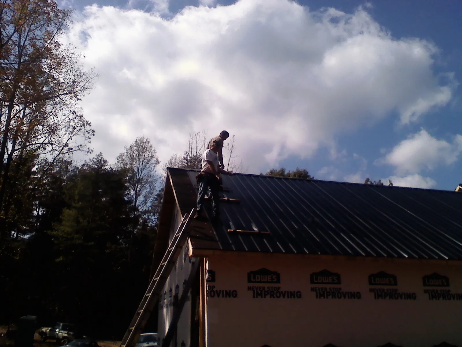 Roofer fastening dark metal panels high against a cloudy sky, from a Roof Inspection job in Powhatan Point