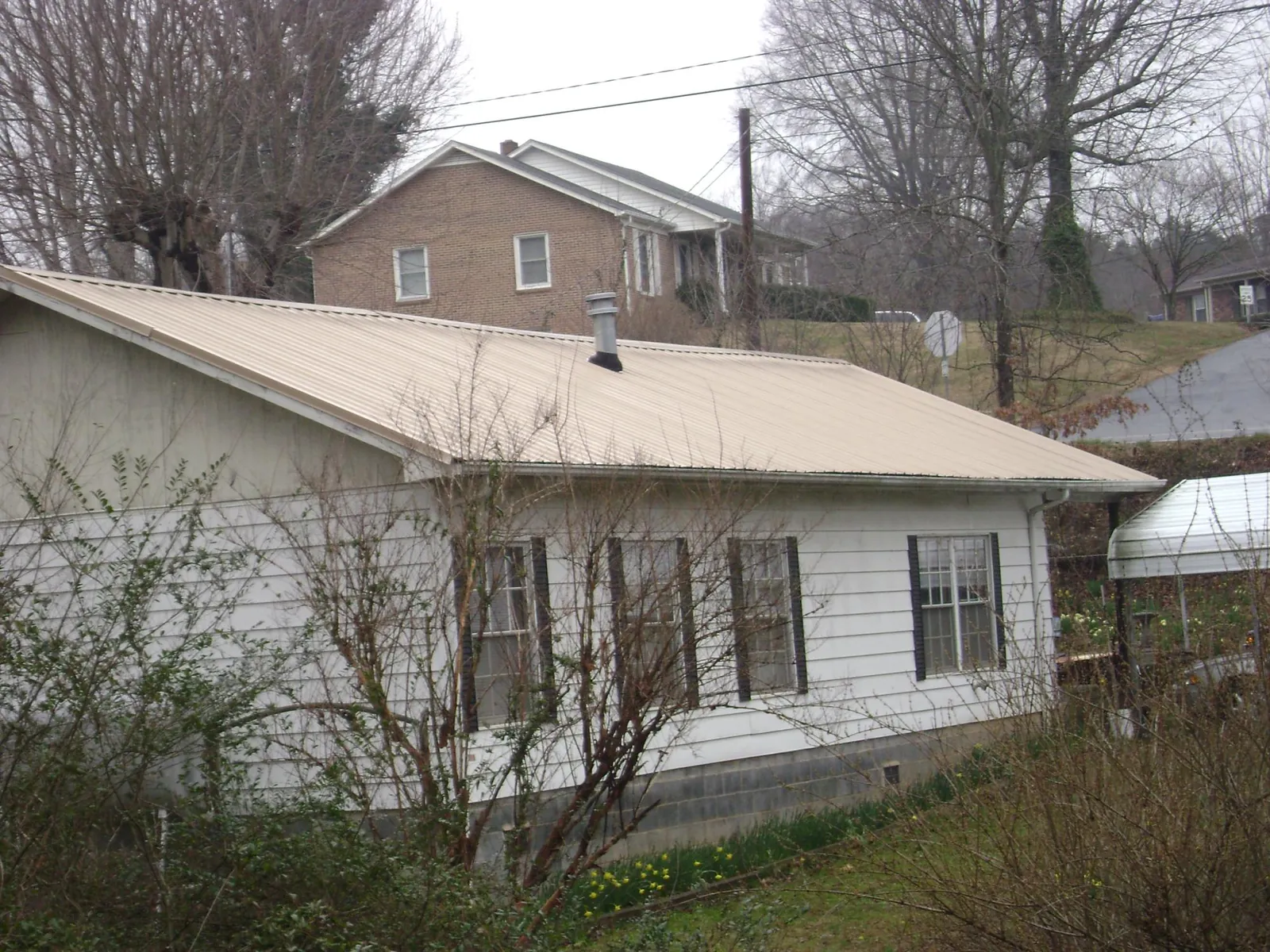 Tan metal roof on a white sided house set into a hillside — Commercial Roofing by Roofing Brothers in Powhatan Point